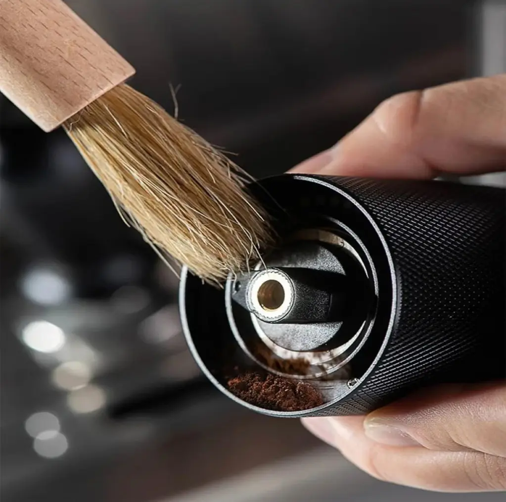 Pincel de limpeza com cabo de madeira e cerdas escuras sendo usado para limpar um moedor de café.