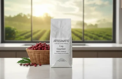 Embalagem de Café Artesanatto Guaxupé ao lado de cesta com grãos vermelhos sobre bancada clara e plantação ao fundo.