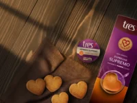 Cápsula e embalagem de Espresso Supremo TRES com biscoitos em formato de coração sobre mesa de madeira ao sol.