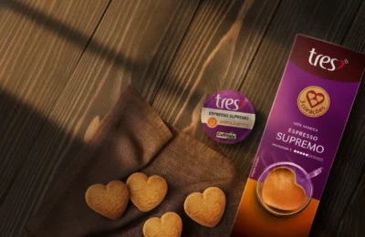 Cápsula e embalagem de Espresso Supremo TRES com biscoitos em formato de coração sobre mesa de madeira ao sol.