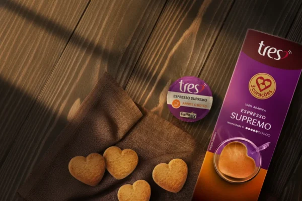 3 Corações Cápsulas Supremo TRES é bom? Vale a Pena em 2026? 7 Cápsula e embalagem de Espresso Supremo TRES com biscoitos em formato de coração sobre mesa de madeira ao sol.