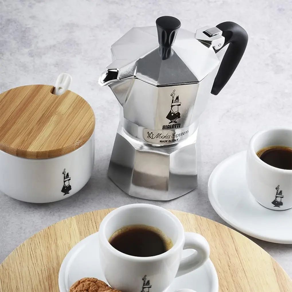 Cafeteira Bialetti Nuova Moka Express prateada sendo montada ou desmontada, com o filtro e a parte inferior visíveis.