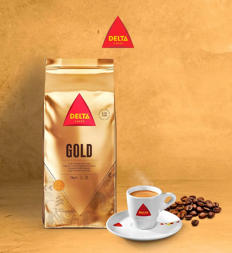 Grãos de Delta Gold Coffee sendo despejados em um moedor de café prateado, sobre uma superfície de madeira escura.