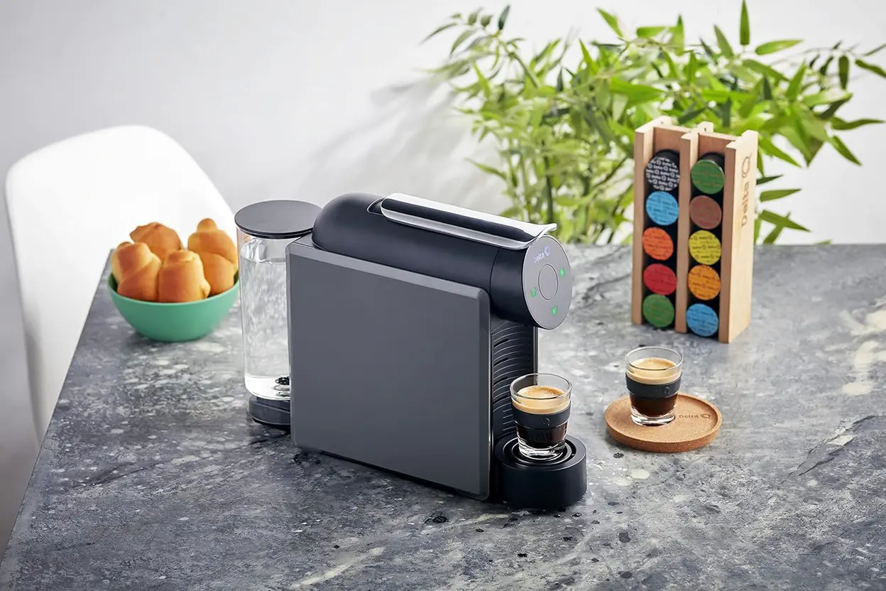 Cafeteira Delta Q MiniQool cinza 220V preparando café em uma xícara branca sobre uma bancada.