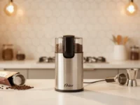 Moedor De Café Oster Inox OMDR na bancada da cozinha com grãos espalhados.